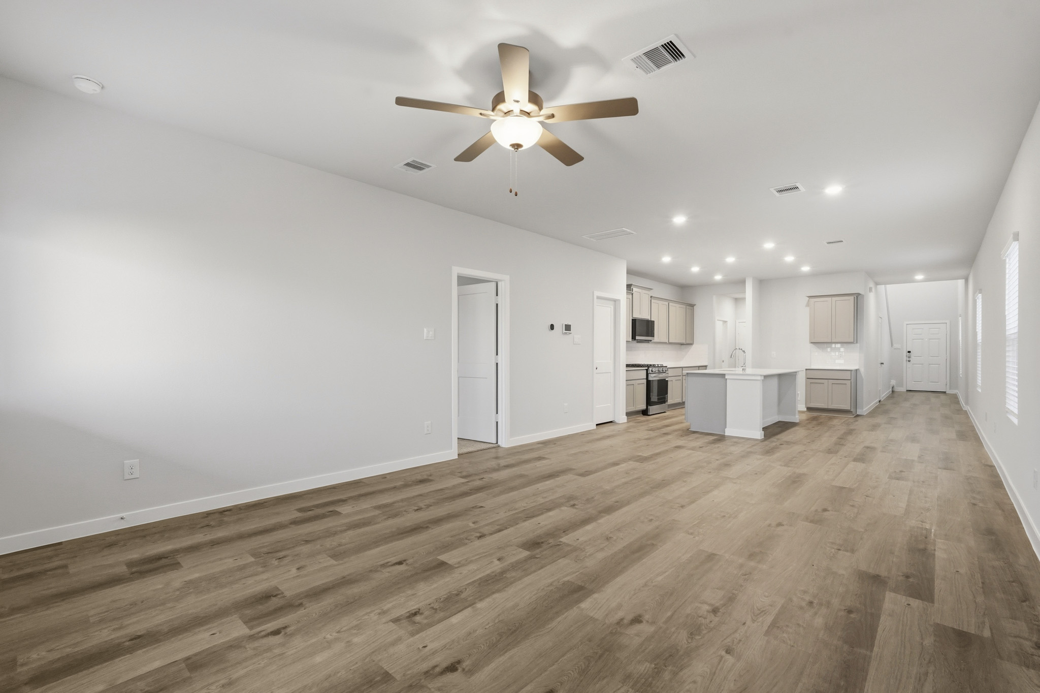 A large empty room with a ceiling fan and a wood floor.