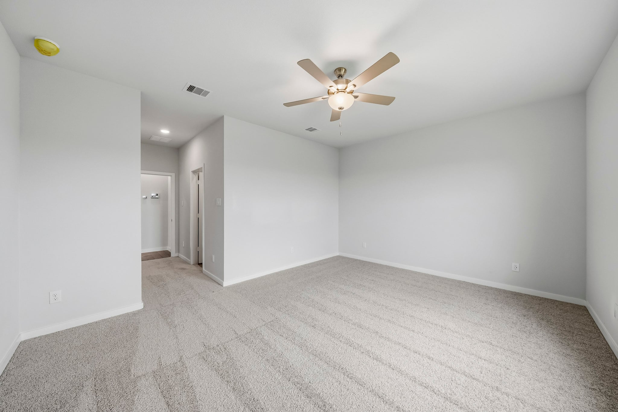 A room with a ceiling fan and a carpet.