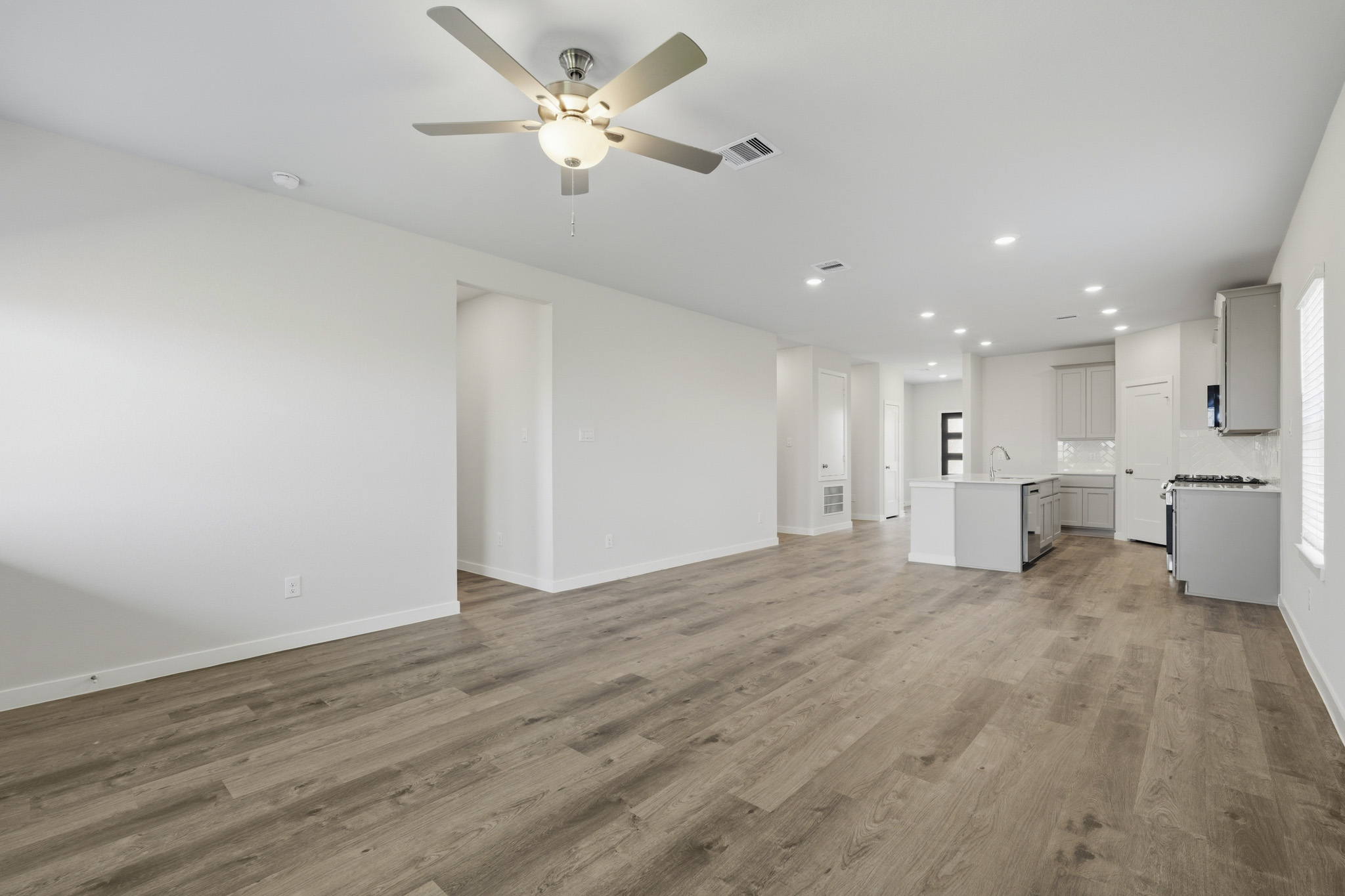 A large empty room with a ceiling fan and a wood floor.