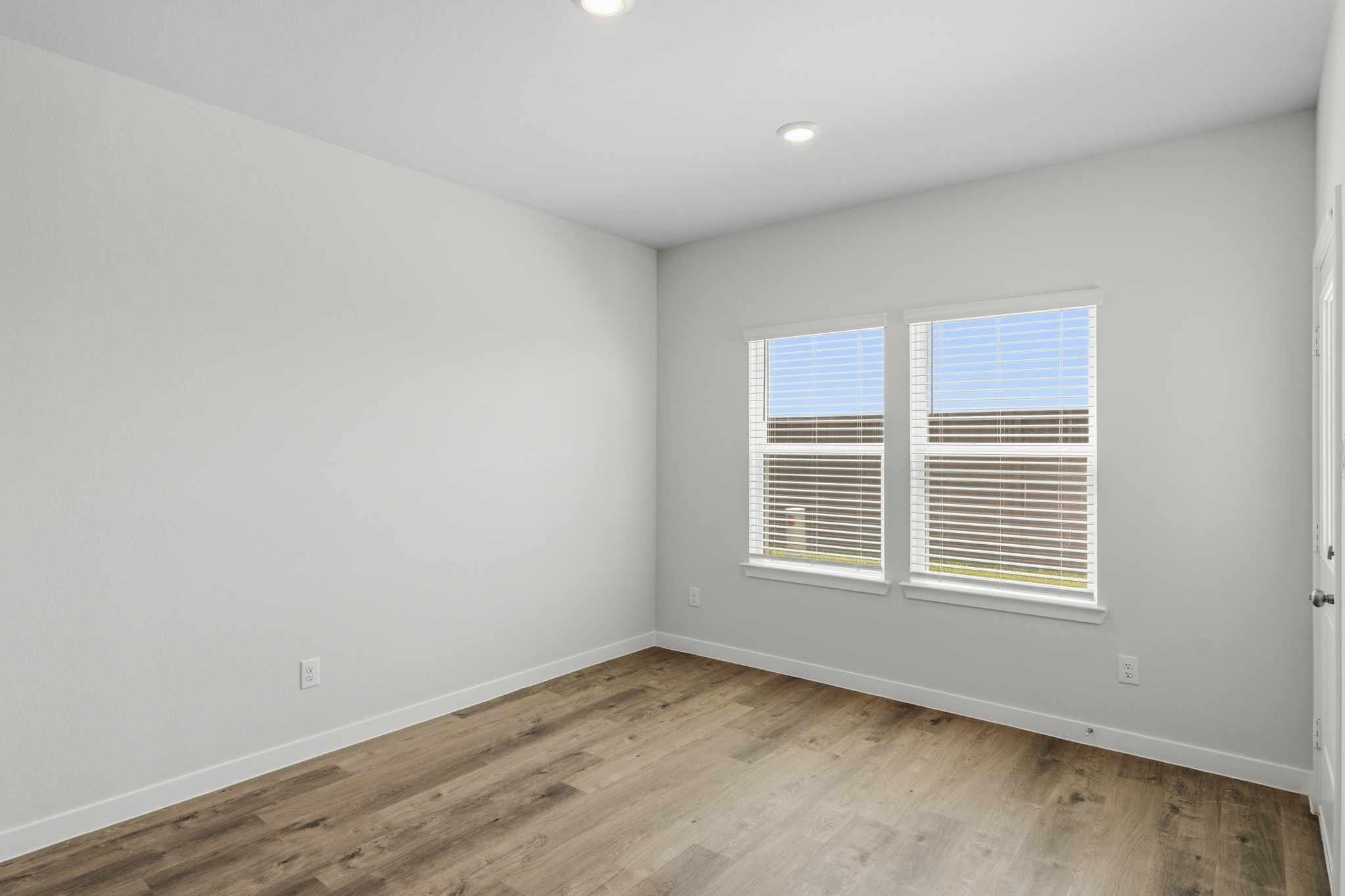 A room with a wood floor and a window with blinds.