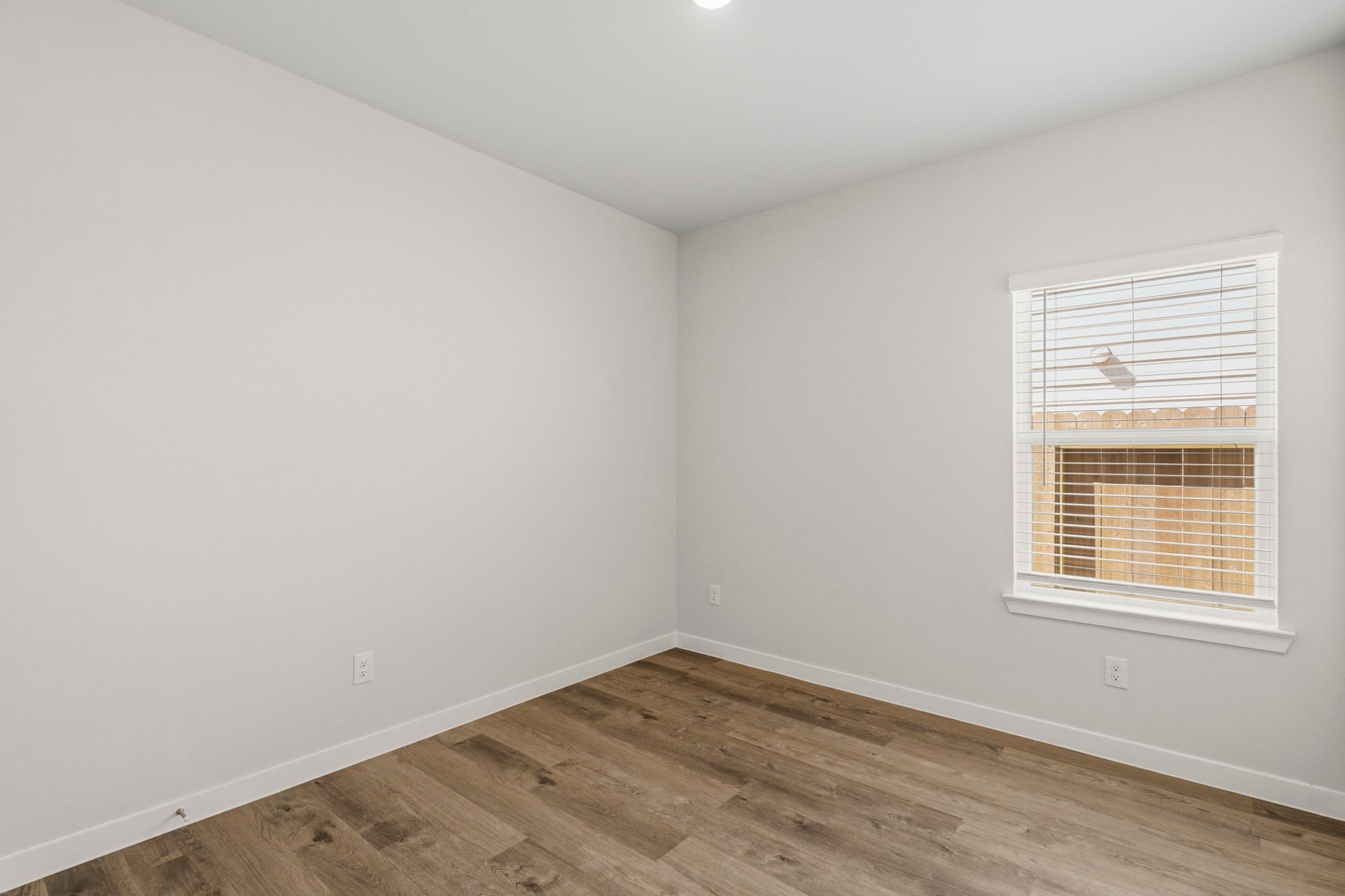 A room with a wood floor and a window with blinds.