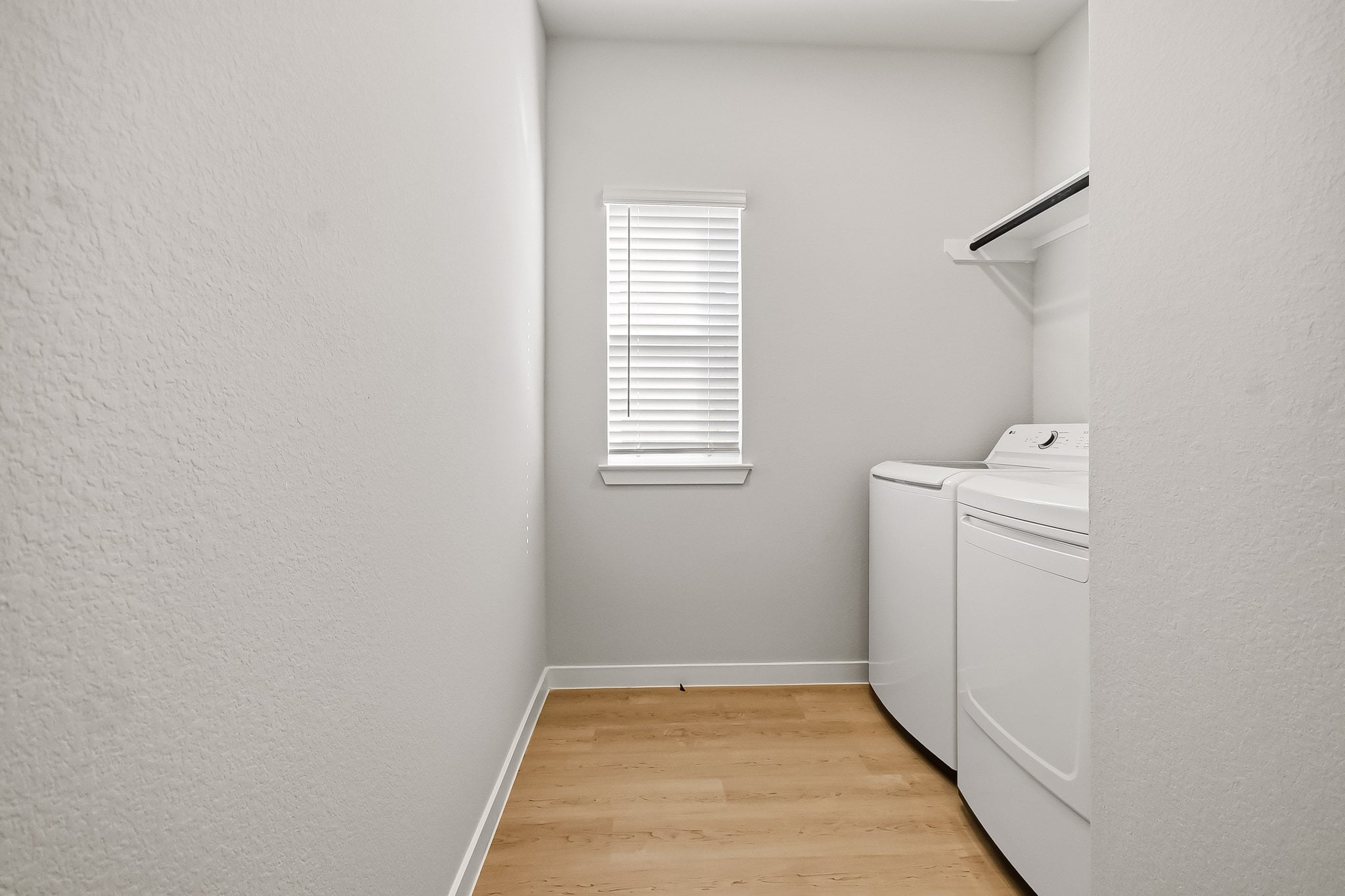 A room with a wood floor and a white wall with a window.