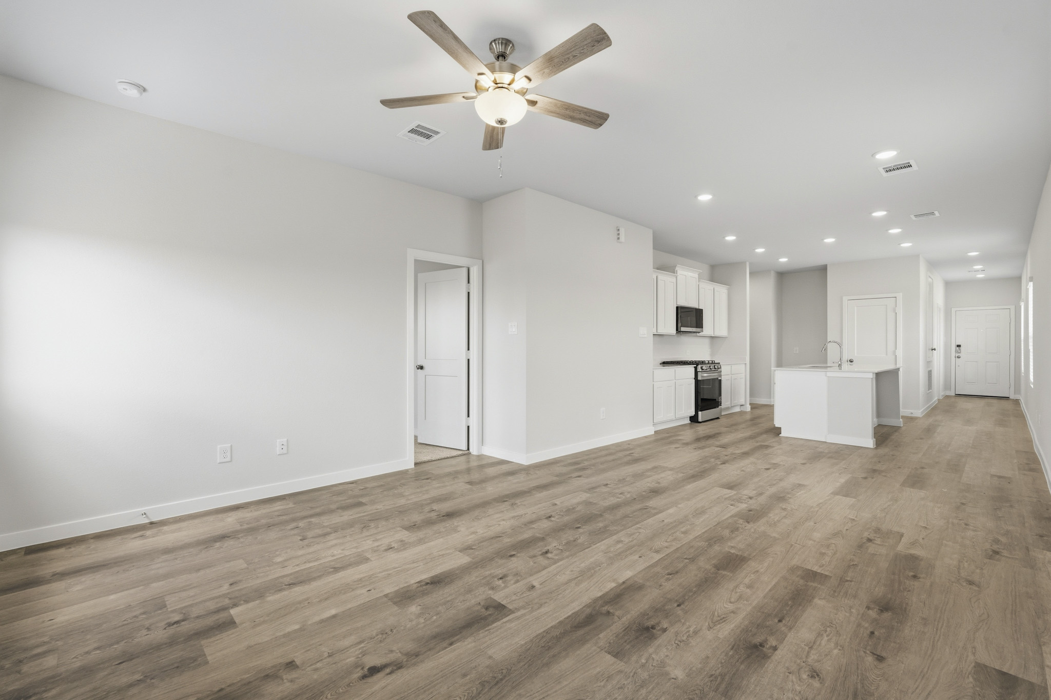 A large empty room with a ceiling fan and white cabinets.
