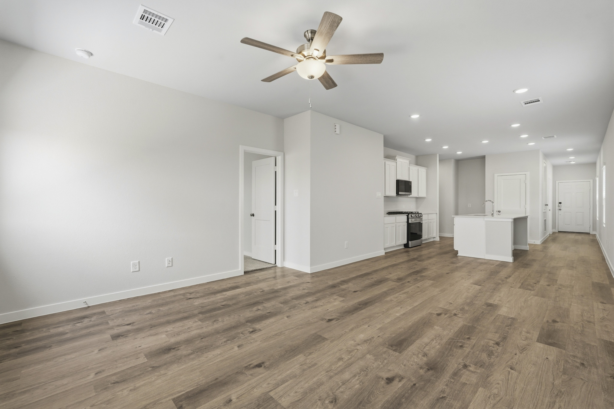 A large empty room with a ceiling fan and white cabinets.