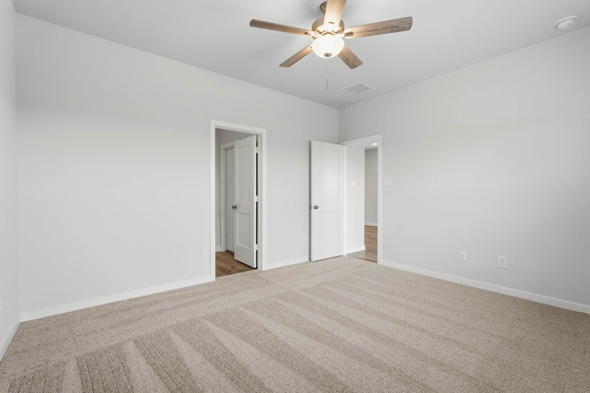 A room with a ceiling fan and a carpet.