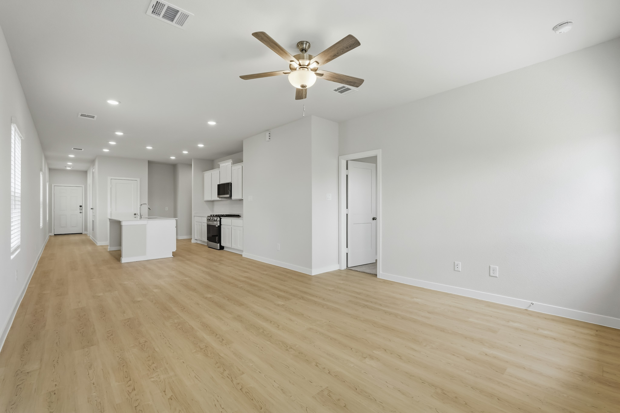 A large empty room with a ceiling fan and white cabinets.