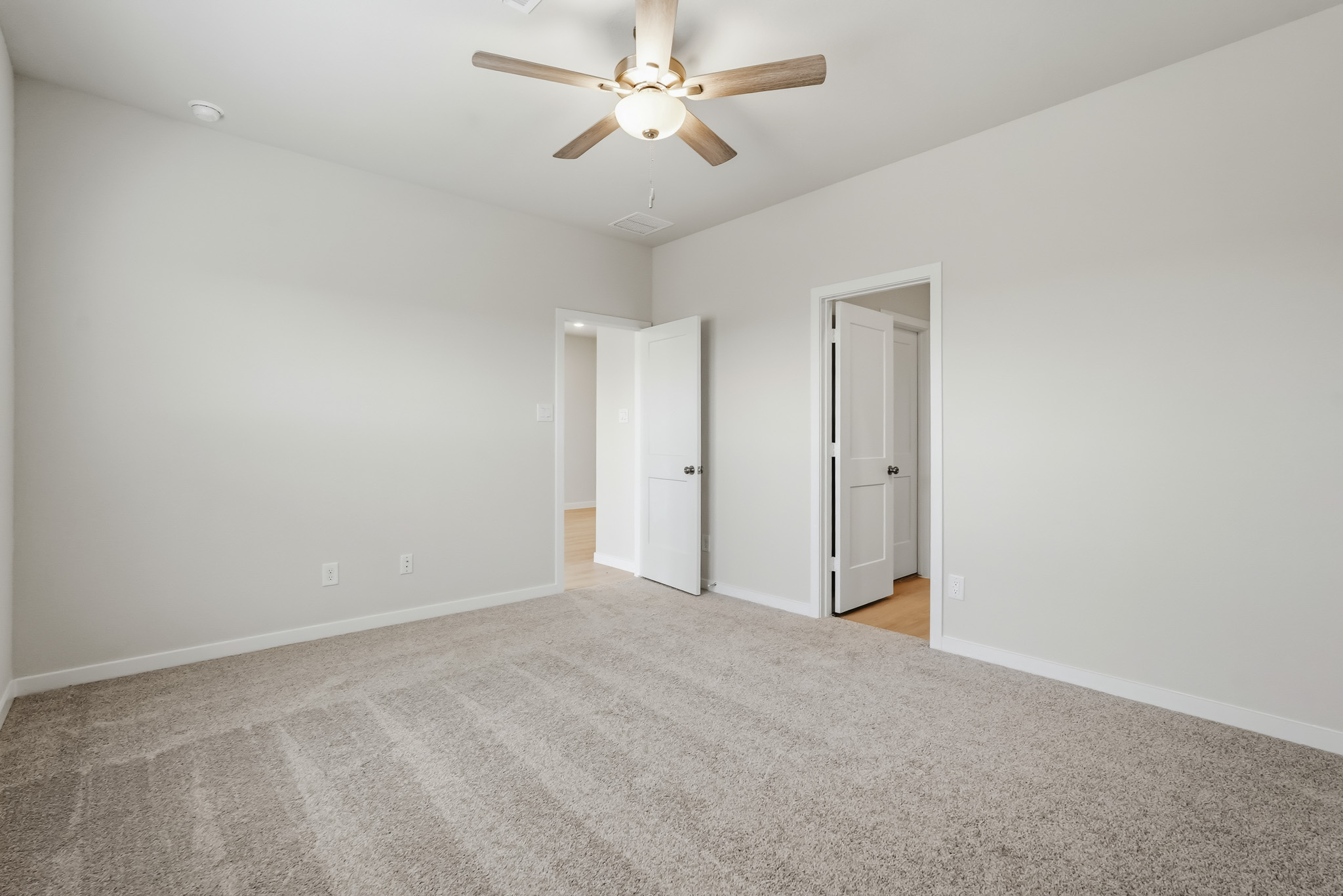 A room with a ceiling fan and a carpet.