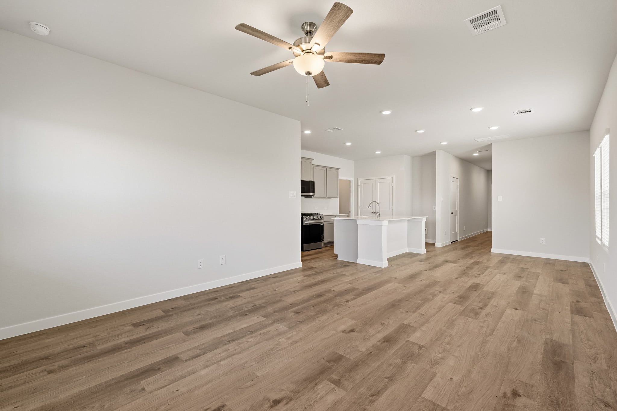 A large empty room with a ceiling fan and a wood floor.