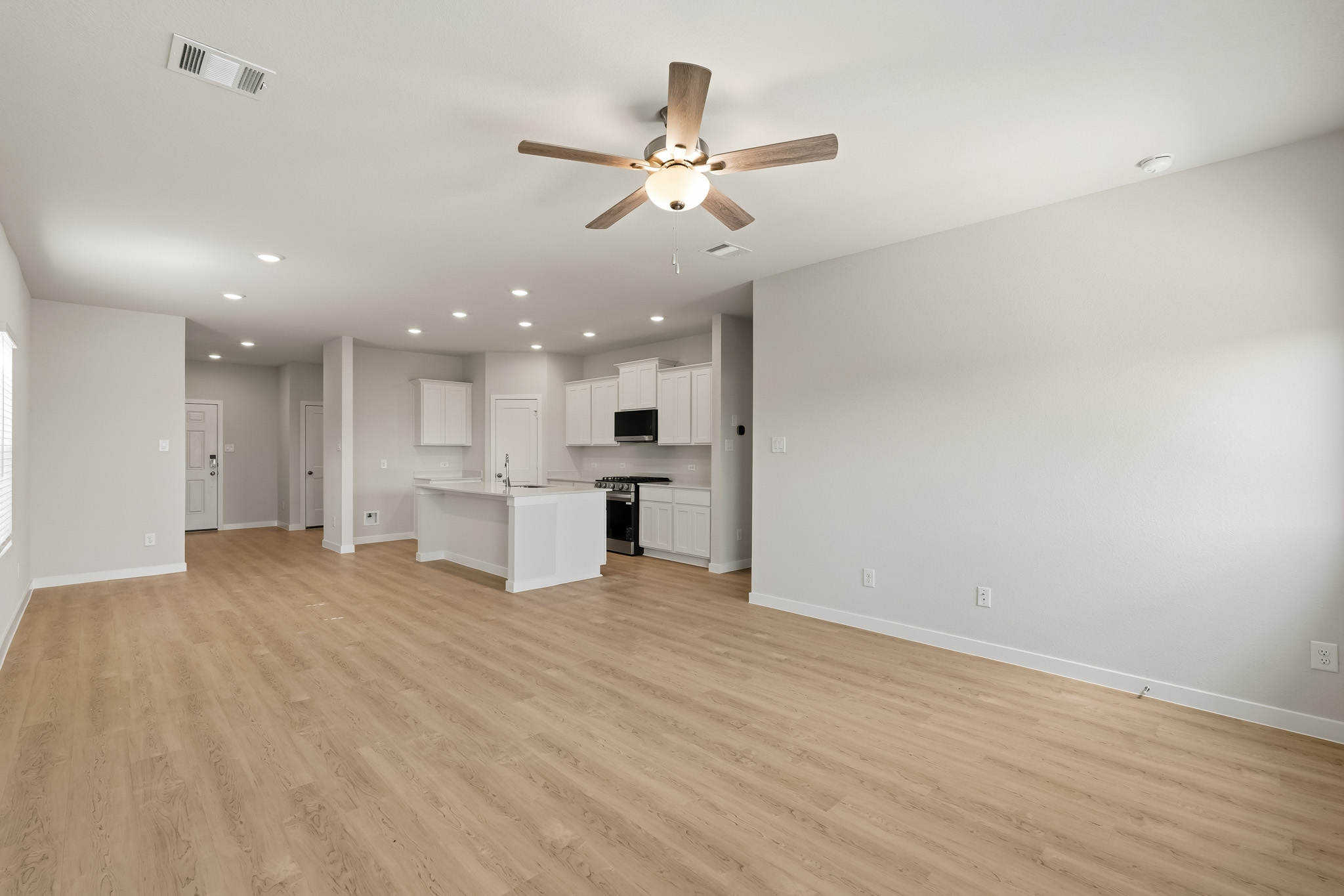 A large empty room with a ceiling fan and a wood floor.
