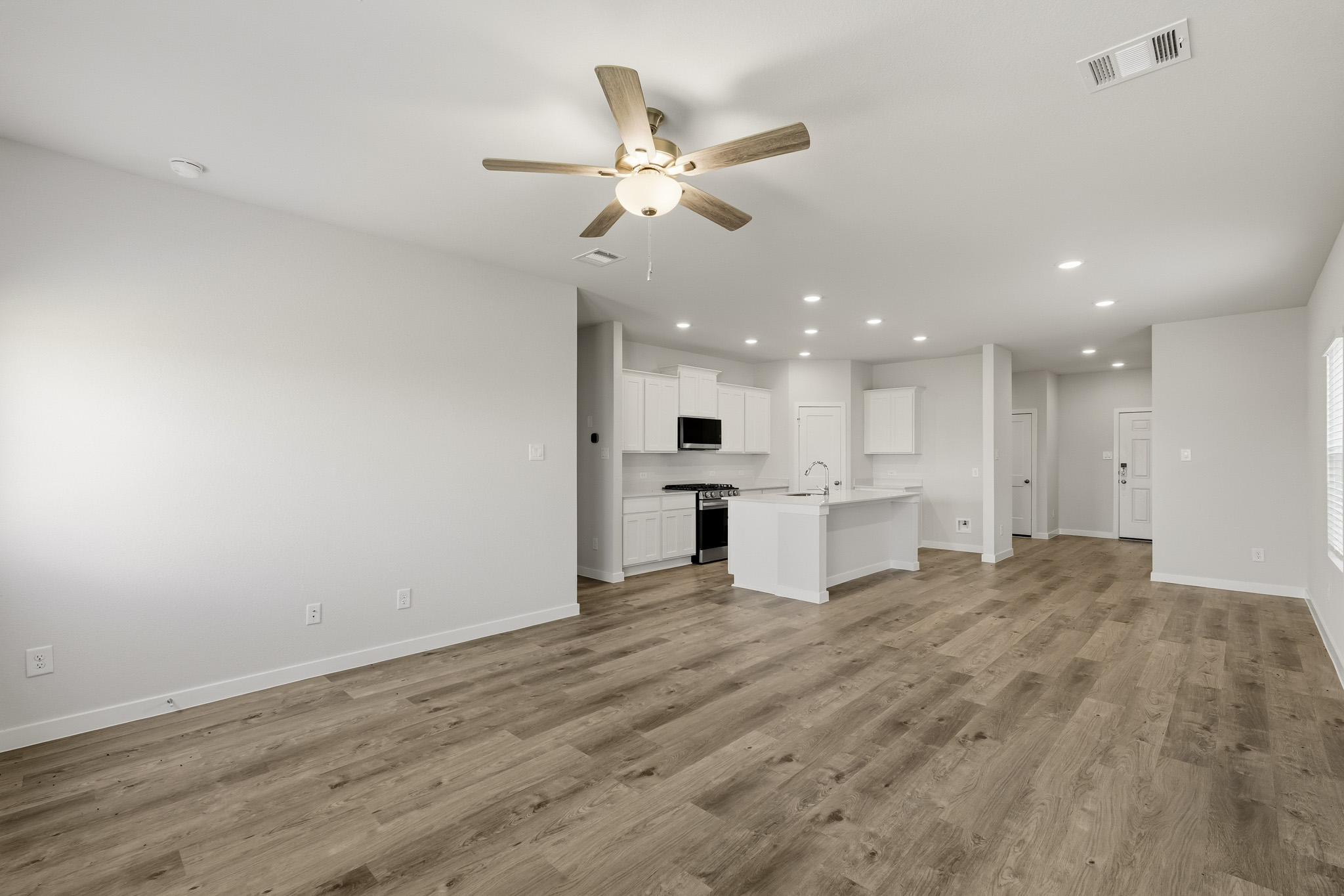 A large empty room with a ceiling fan and a wood floor.