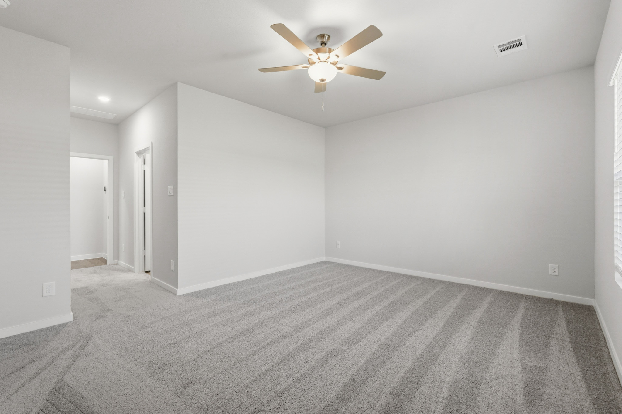 A room with a ceiling fan and a carpet.