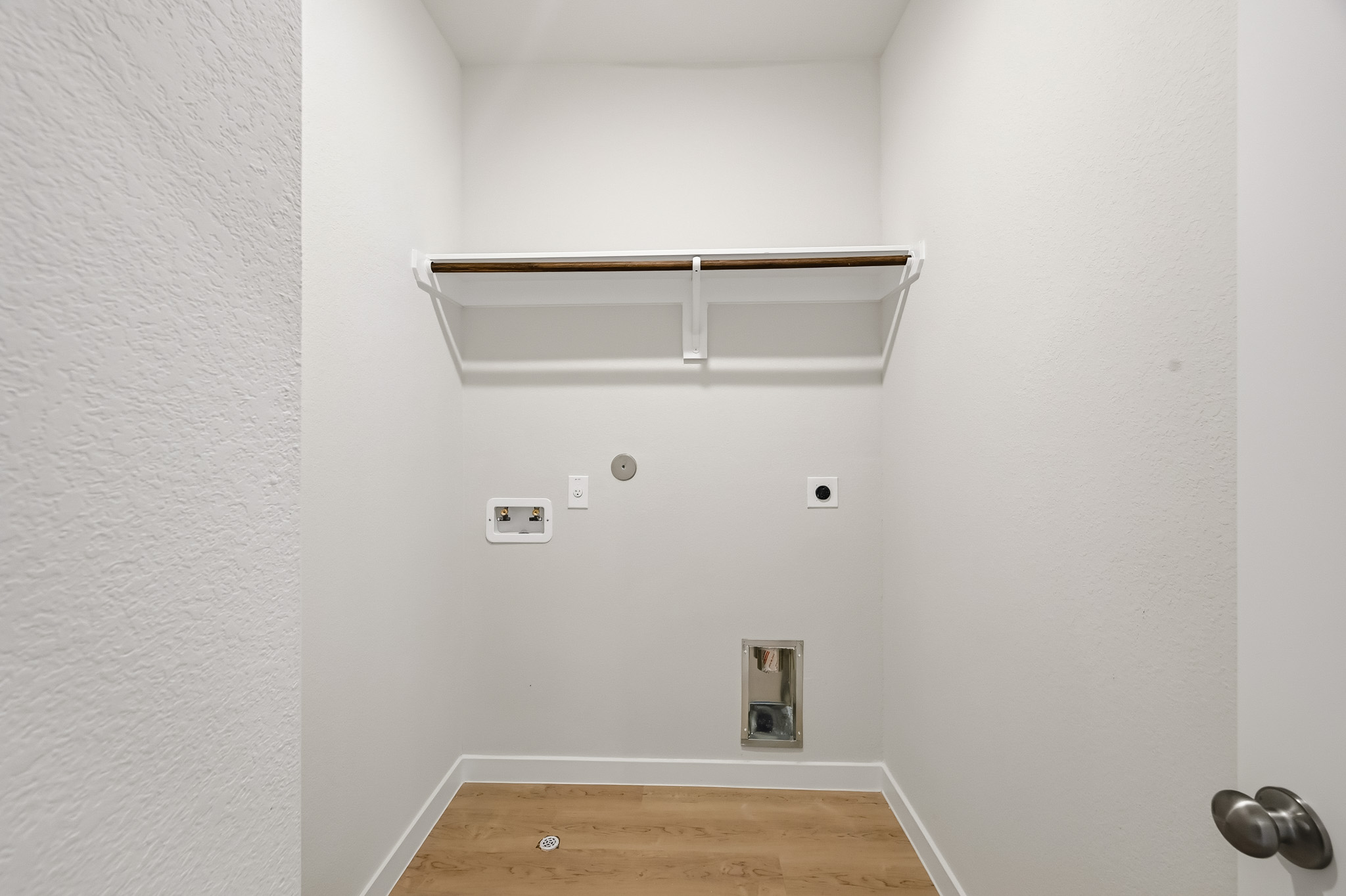 A white room with a wood floor and a white wall with a light.