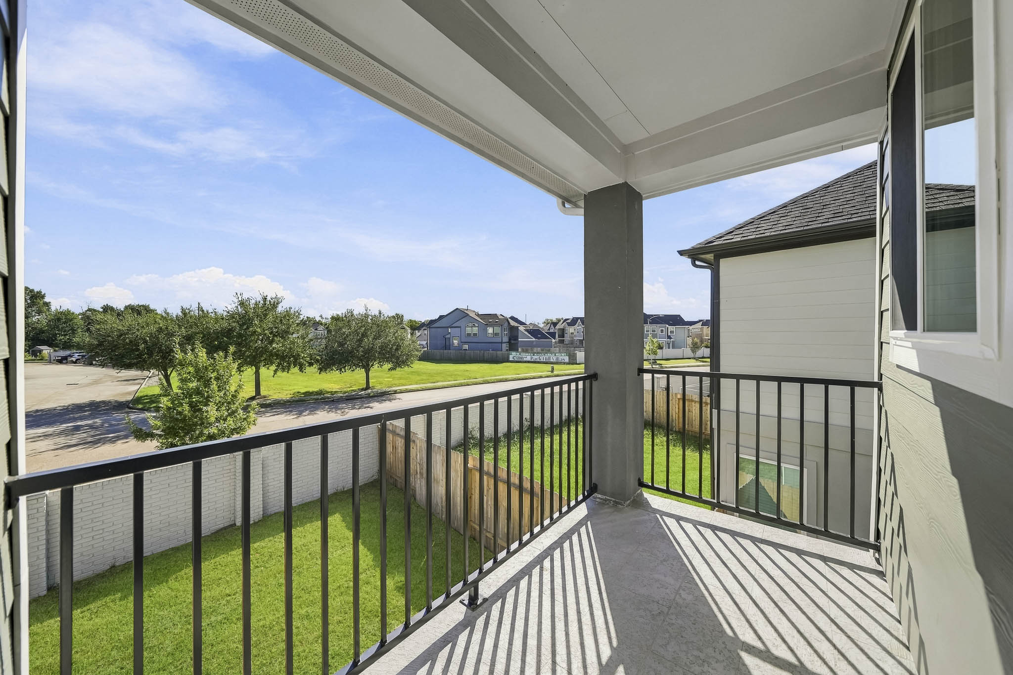 A deck with a railing and grass and trees and a building in the background.