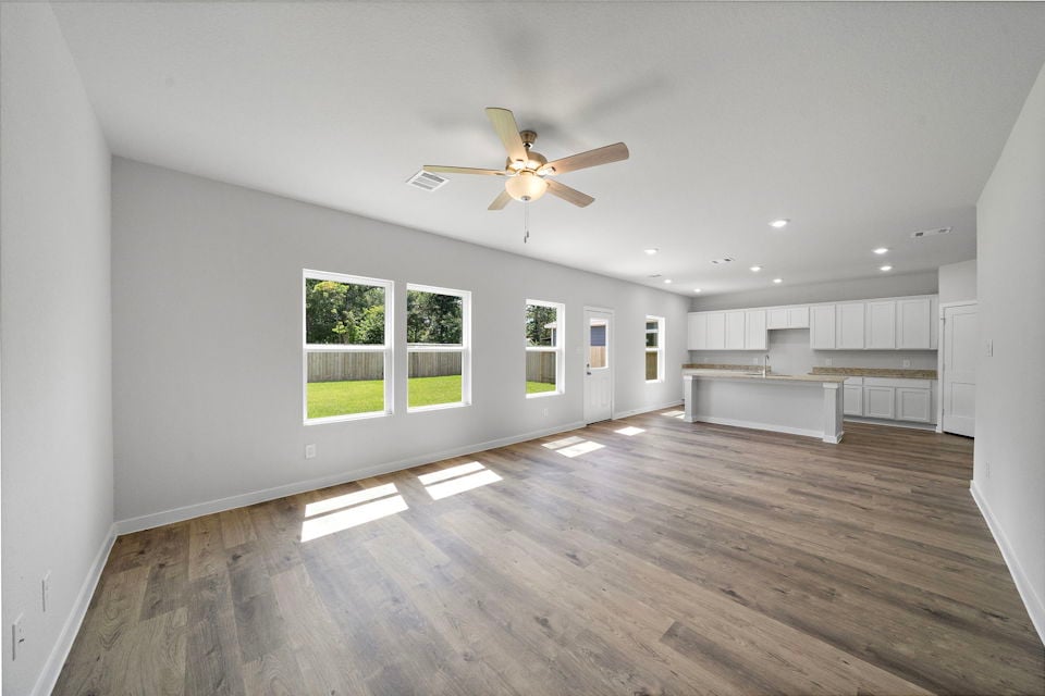 A large empty room with a ceiling fan and a wood floor.