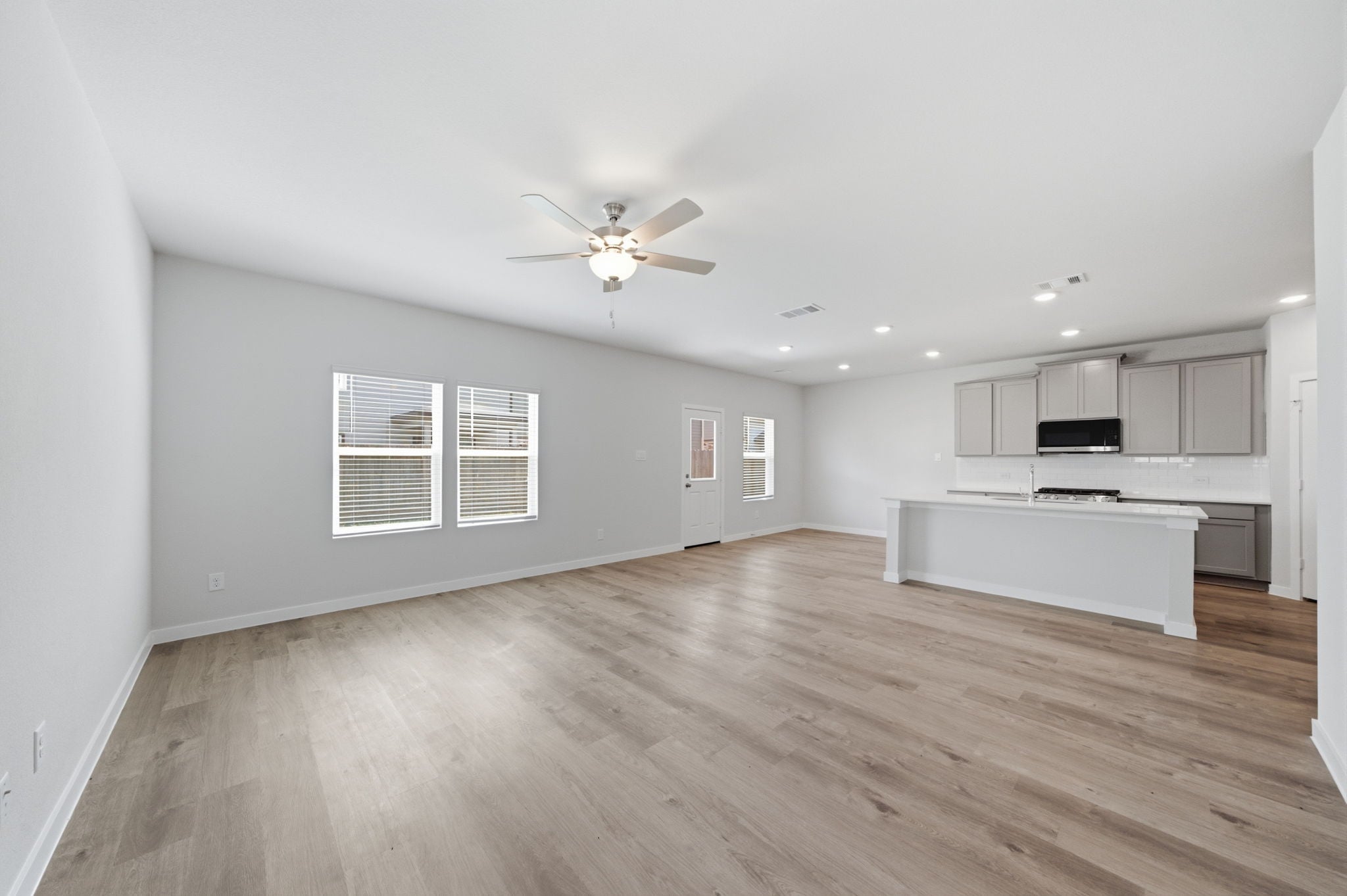 A large empty room with a wood floor and a ceiling fan.