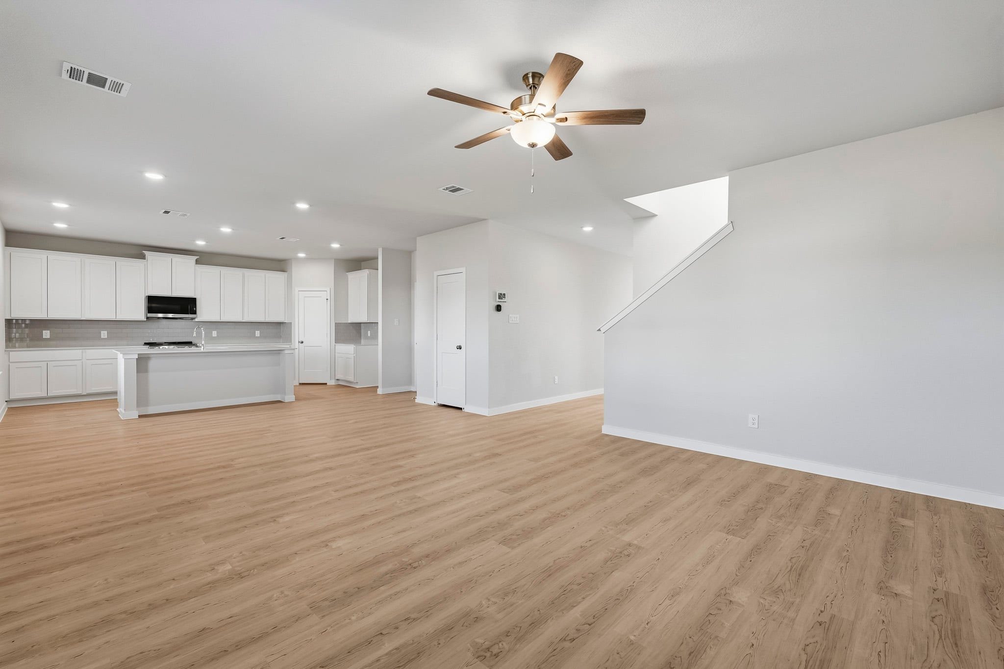 A large empty room with a ceiling fan and white cabinets.
