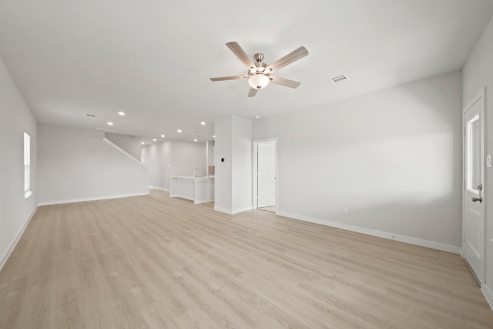 A large empty room with a ceiling fan and a wood floor.