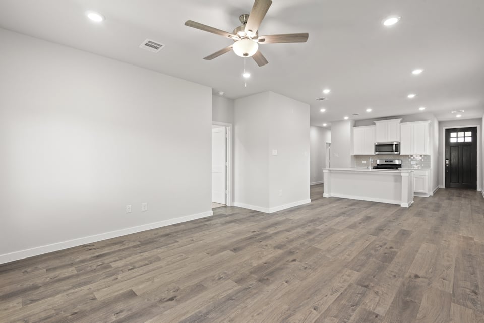 A large empty room with a ceiling fan and a wood floor.