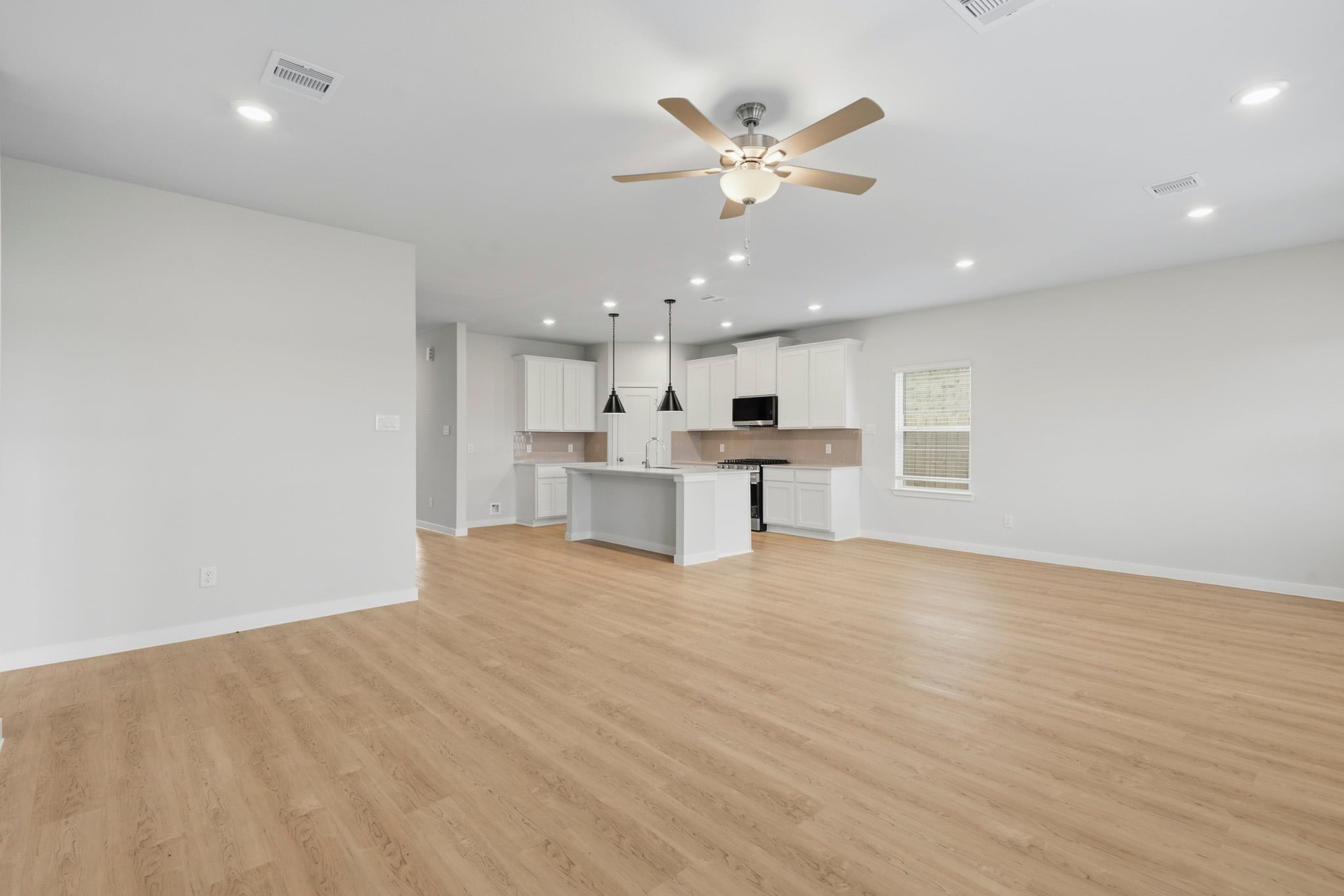 A large empty room with a ceiling fan and a wood floor.