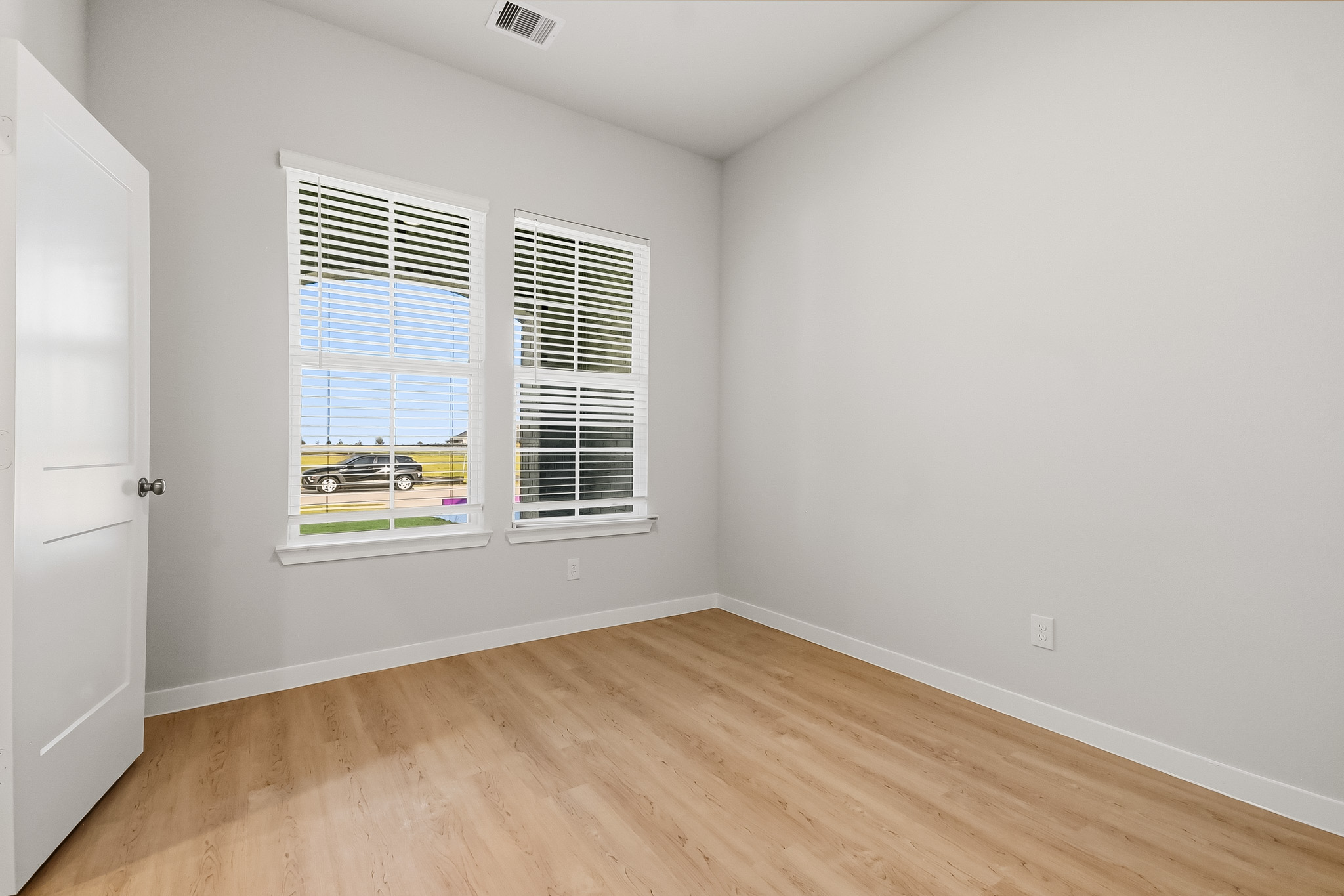 A room with a wood floor and a window with blinds.