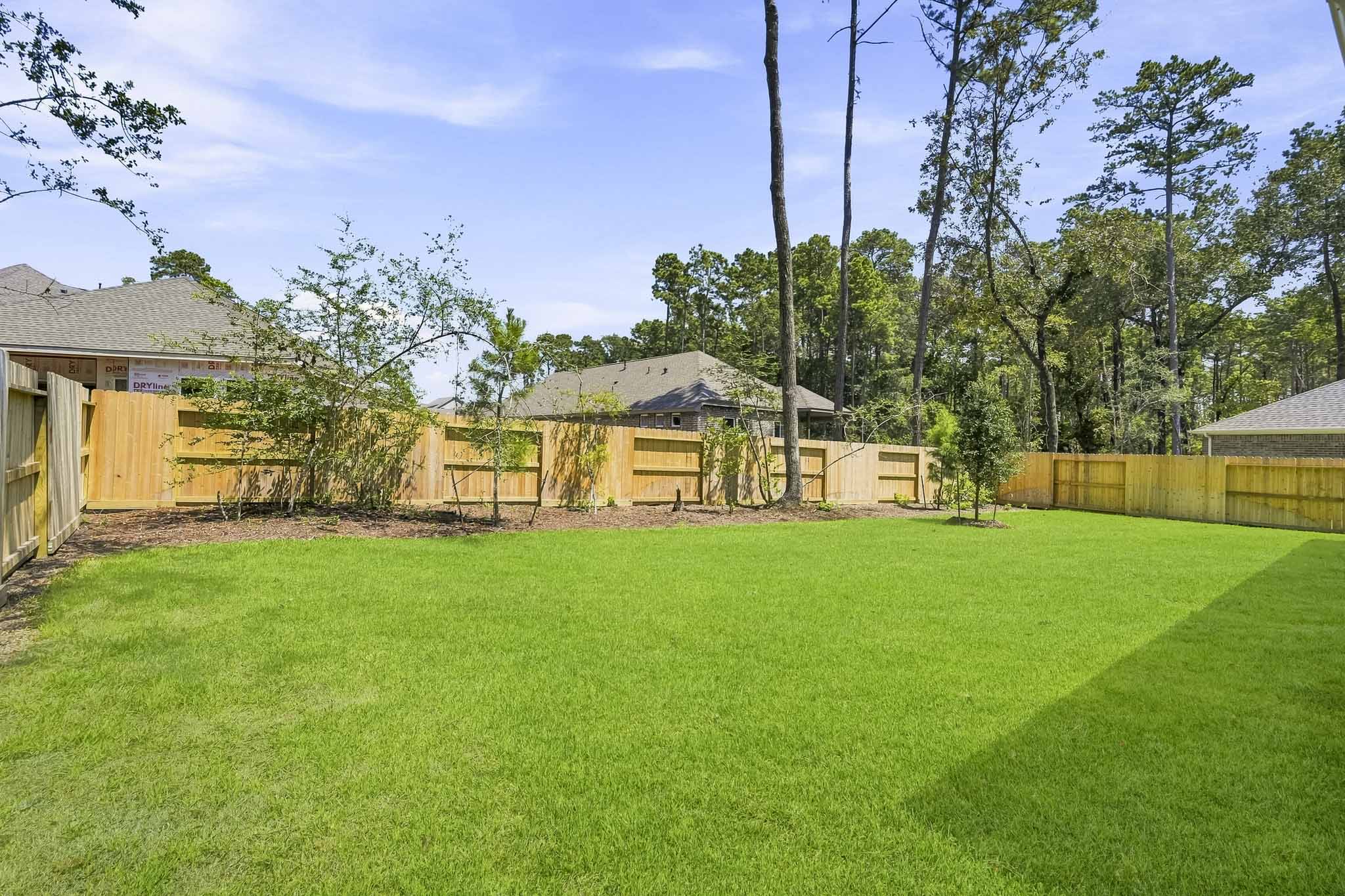A grassy yard with trees and a fence.