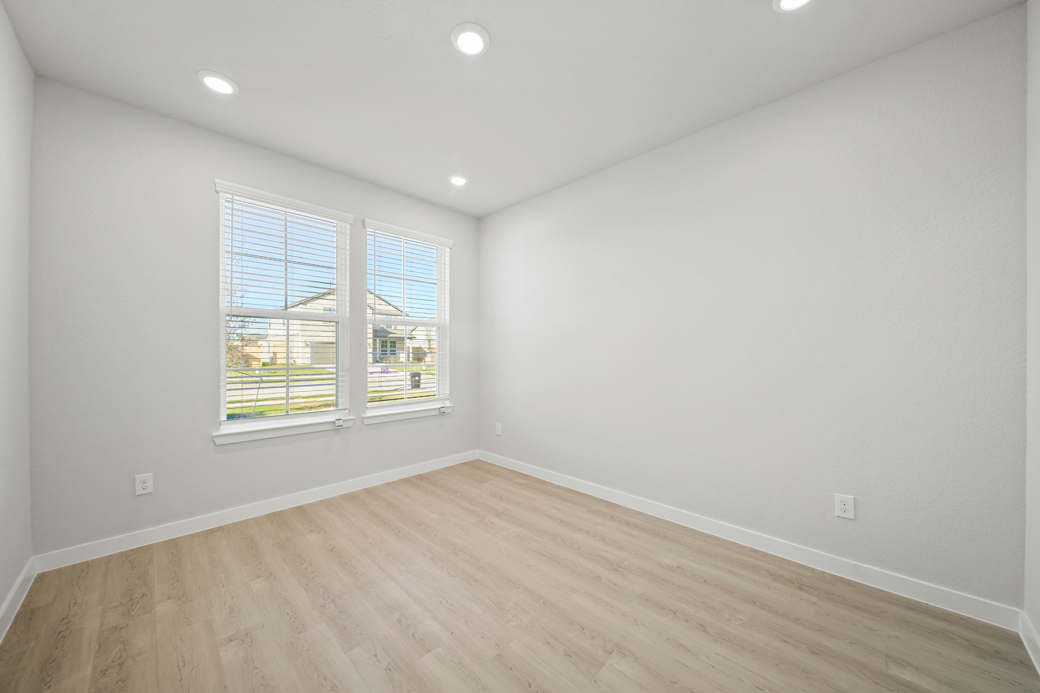 A room with a wood floor and a window with blinds.