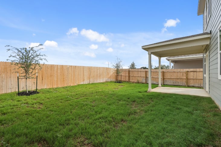 A fenced in yard with a tree and a house in the background.