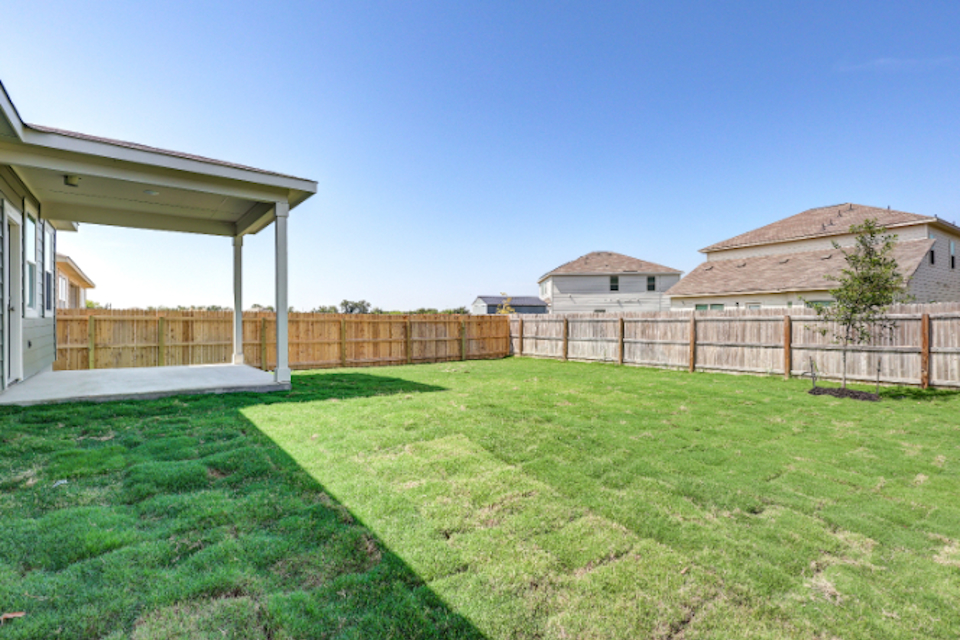 A fenced in yard with a house and a tree.