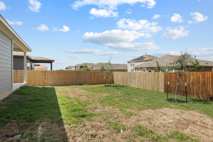 A fenced in yard with a dirt yard and a house in the background.