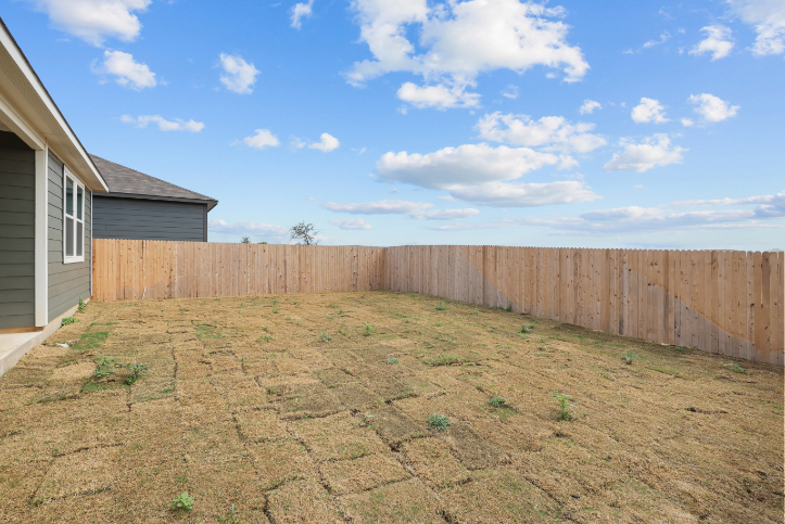 A fenced in yard with a dirt patch and a house.