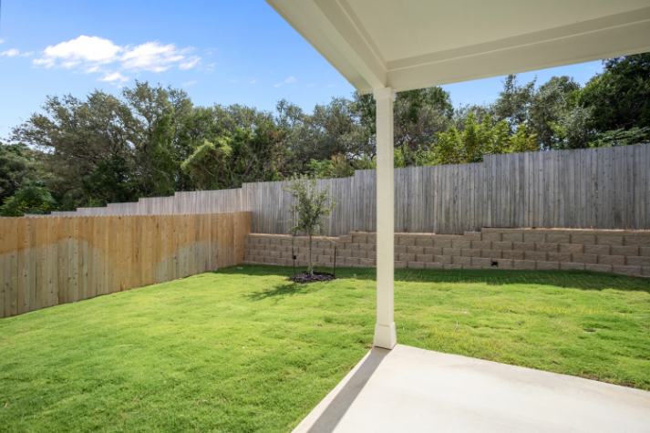 A covered patio with a fence and a tree in the background.