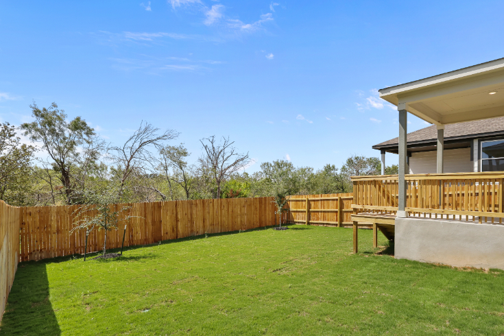 A fenced in yard with a house and trees in the background.