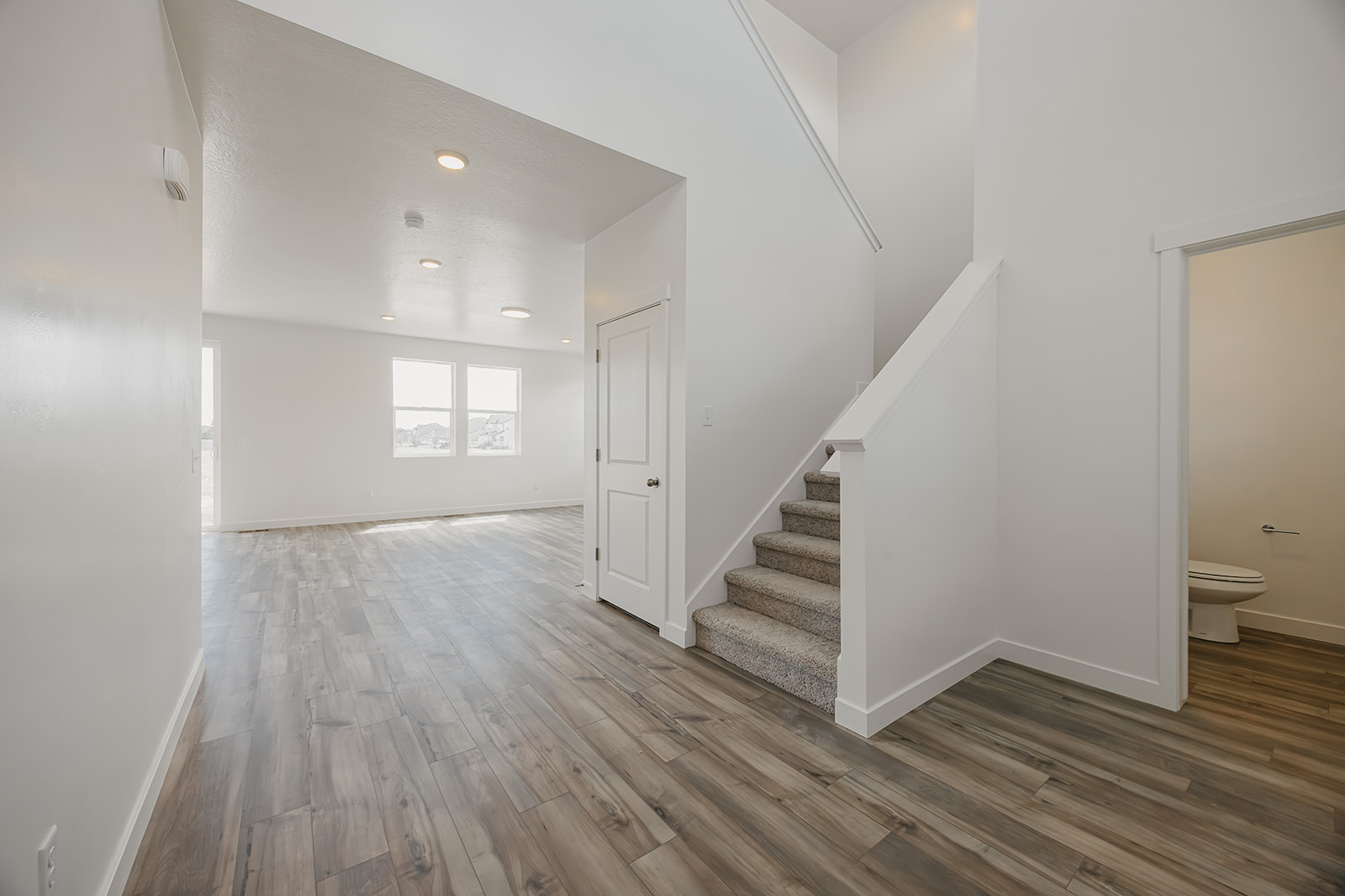 A large white room with a wood floor and a toilet.