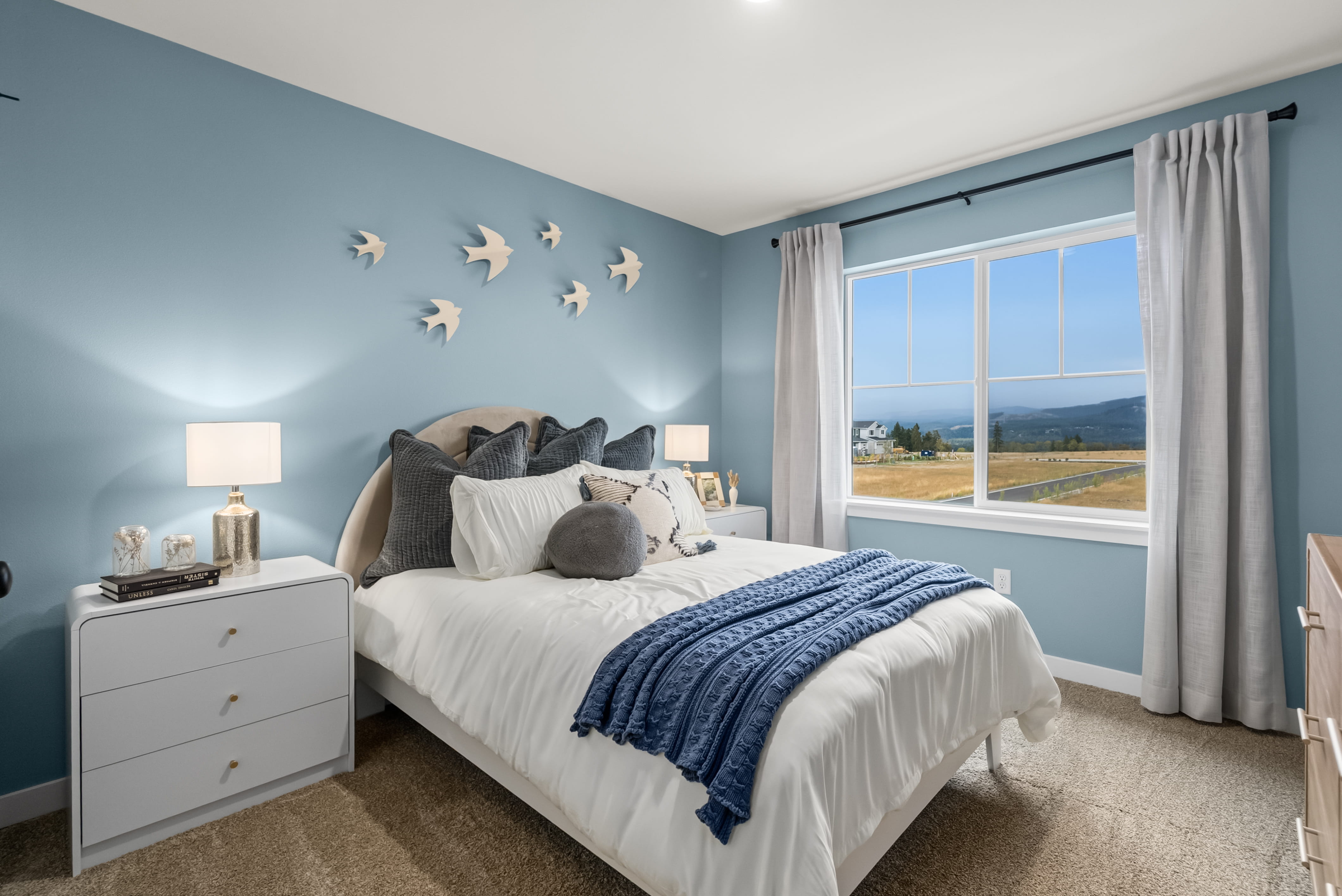 A bedroom with a bed and a window with birds flying.