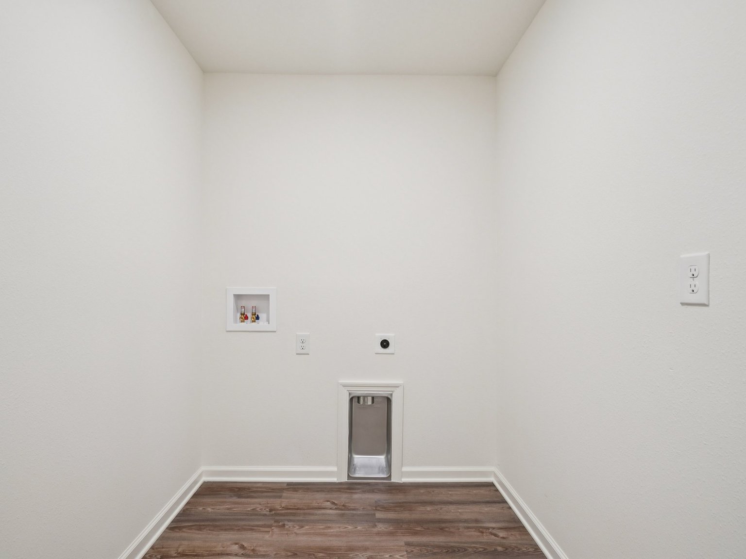 A room with a wood floor and a white wall with a door.