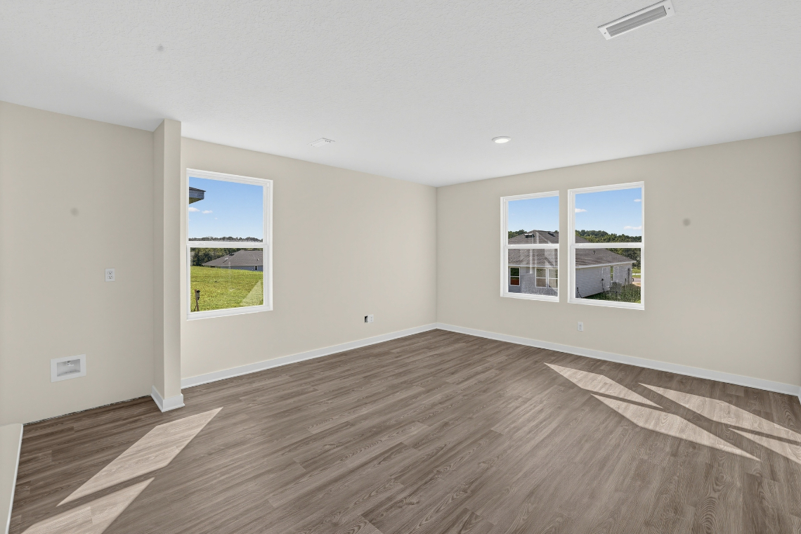A room with a wood floor and a window with a view of the grass and a building.