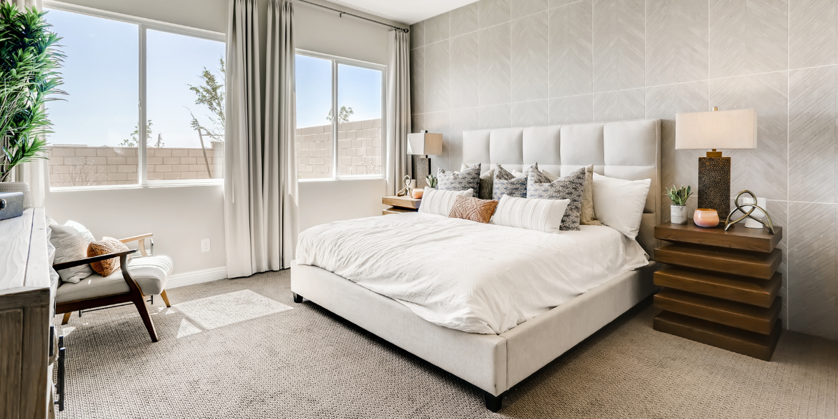 Generous owner’s suite with grey accent wall, white bedding, large windows and a seating area. 