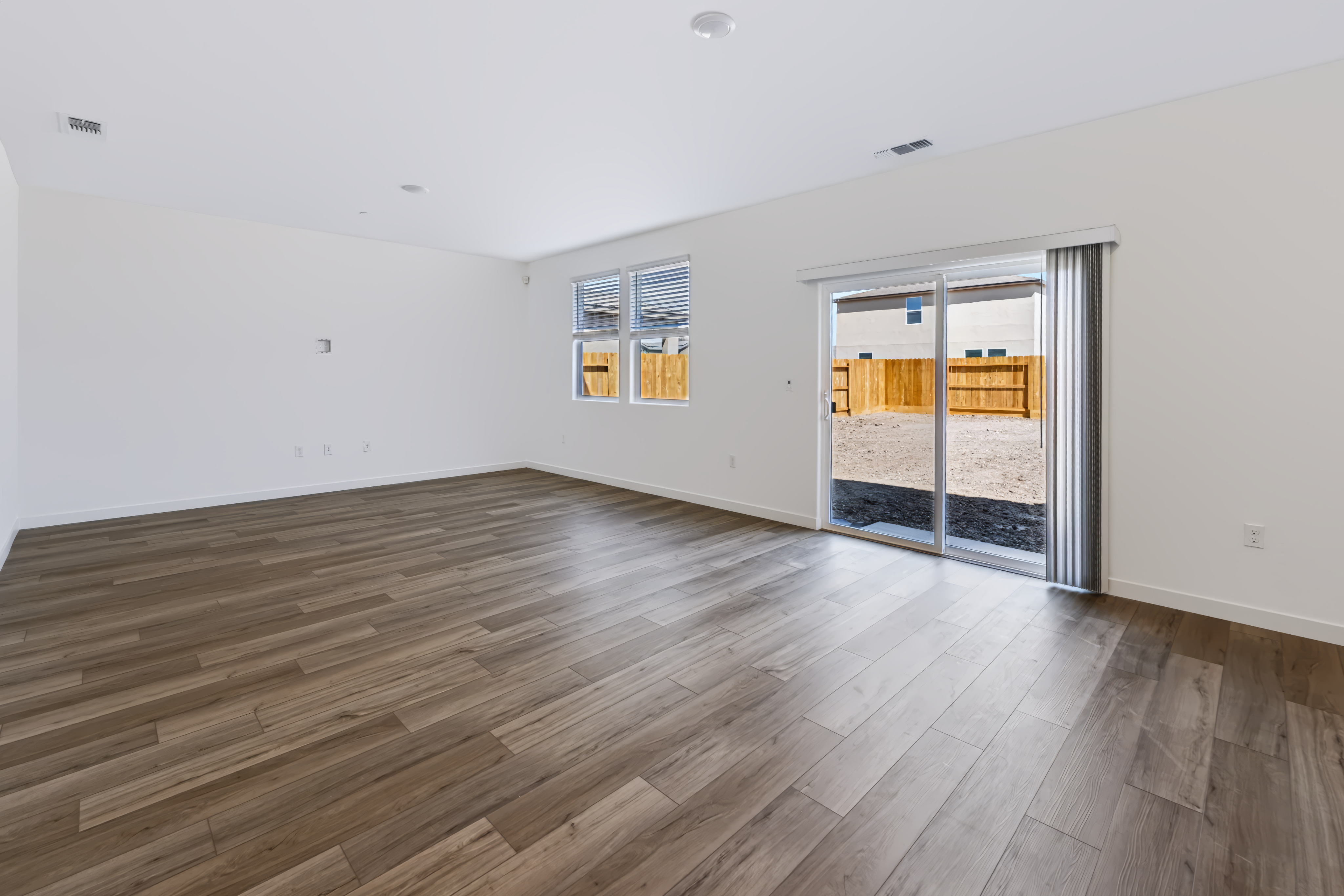 A room with a wood floor and a wood floor with a bed and a window with blinds.