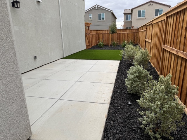 A backyard with a fence and bushes.