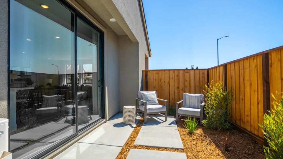 A patio with chairs and a glass door with a wood fence and a wood fence and a blue.